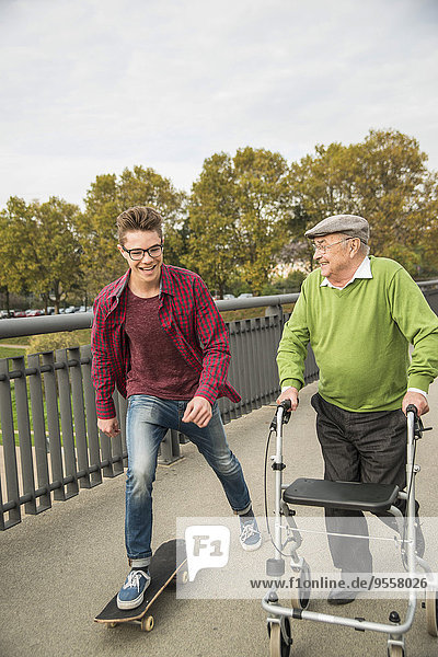 Fröhlicher Senior mit Rollator und erwachsenem Enkel mit Skateboard