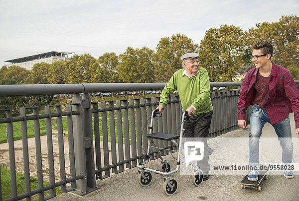 Fröhlicher Senior mit Rollator und erwachsenem Enkel mit Skateboard