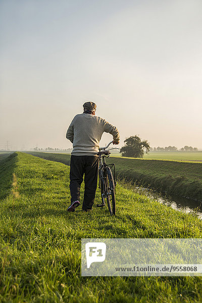 Senior man in rural landscape pushing bicycle