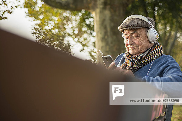 Senior auf Parkbank mit Handy und Kopfhörer