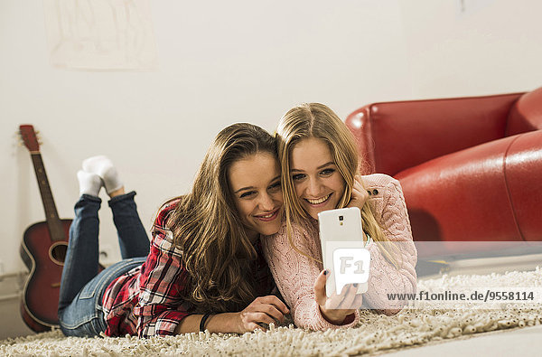 Two female friends taking a selfie with smartphone at home