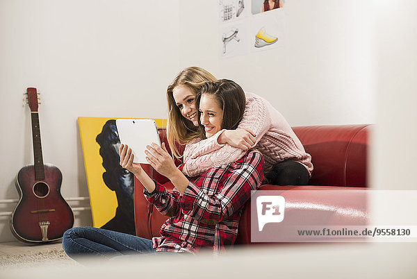 Two female friends using digital tablet at home