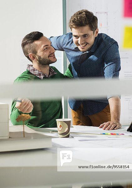Two smiling young men in office with architectural model