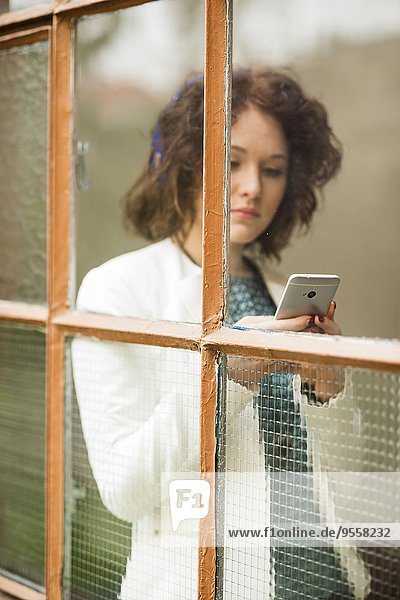 Junge Geschäftsfrau mit Handy hinter dem Fenster