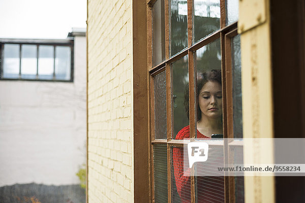 Young woman with cell phone behind window