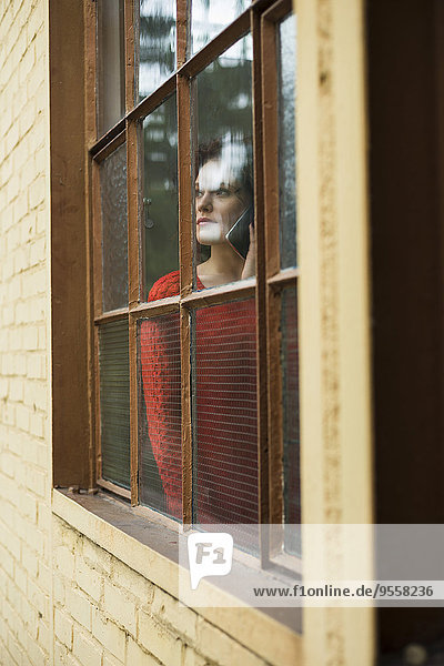 Young woman on cell phone behind window