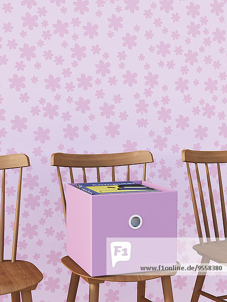 Stuhl mit Bücherkarton vor rosa Tapete mit Blumenmuster