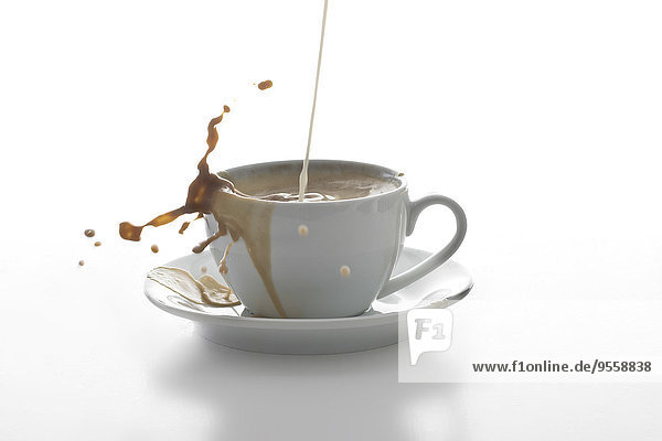 Milch spritzend in einer Tasse Kaffee vor weißem Hintergrund