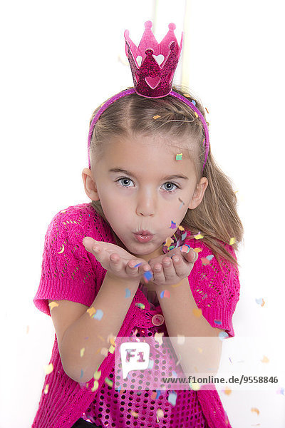 Porträt eines kleinen Mädchens  das sich als Prinzessin verkleidet und Konfetti bläst.
