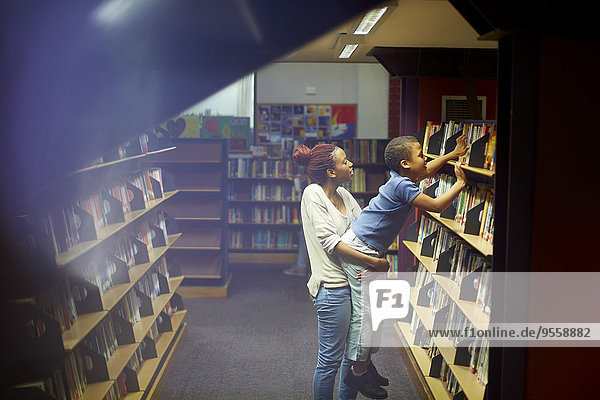 Junge Frau hält Junge am Bücherregal in der Bibliothek