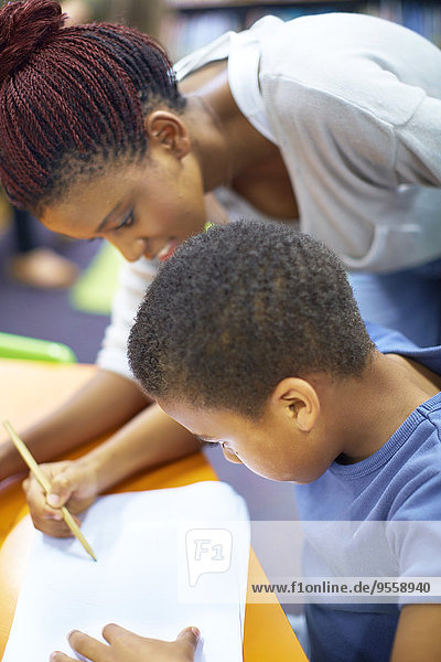 Junge Frau unterrichtet den Jungen beim Schreiben auf Papier