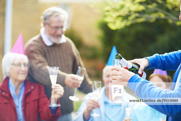 Senior Mann gießt Champagner ins Glas auf einer Geburtstagsgartenparty