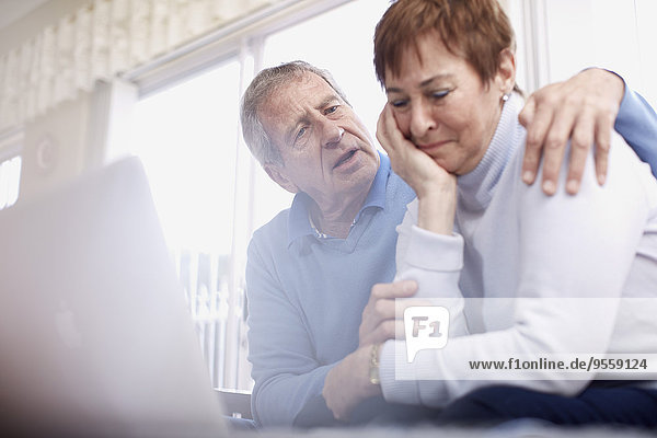 Senior man consoling crying wife at laptop