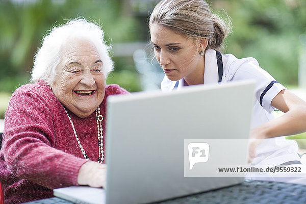 Krankenschwester und Seniorin nutzen gemeinsam den Laptop