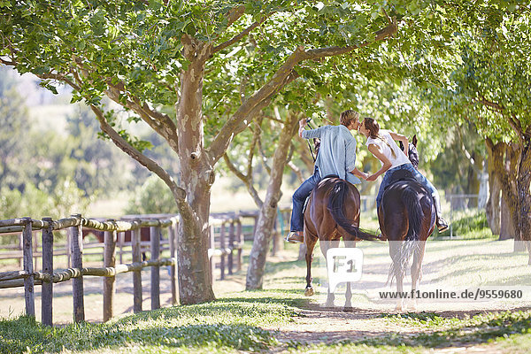 Young couple on horses kissing at paddock