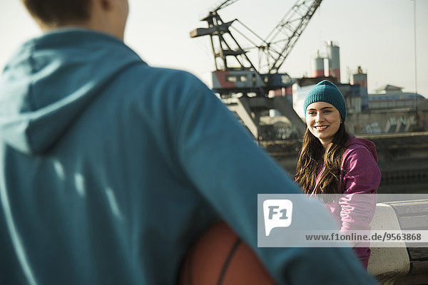 Außenaufnahme Jugendlicher sehen lächeln Junge - Person halten Basketball Kleidung Mütze Mädchen Industriegebiet freie Natur