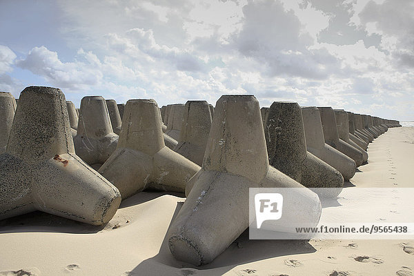 Tetrapod rocks arranged on sandy beach against cloudy sky
