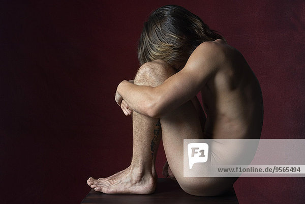 Nackter Mann sitzend in fetaler Position  Seitenansicht