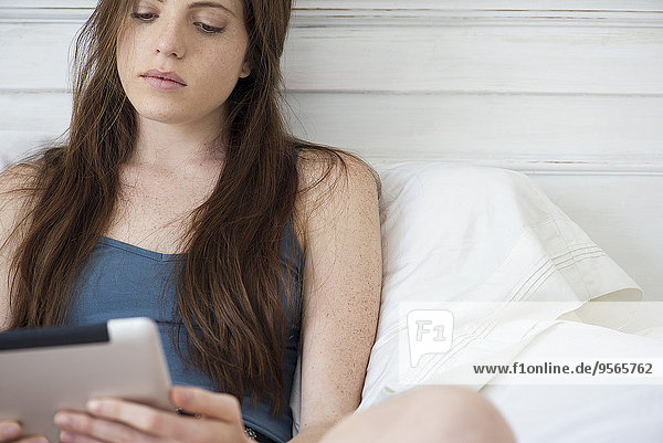 Frau im Bett sitzend mit digitalem Tablett