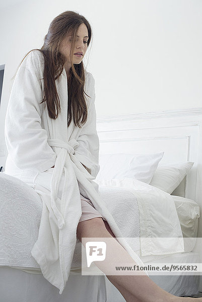 Woman wearing bathrobe sitting on edge of bed