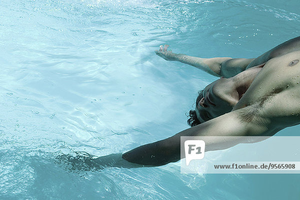 Mann lehnt sich rückwärts über das Schwimmbad  baumelt mit den Armen im Wasser.