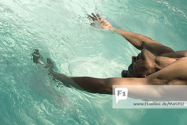 Mann lehnt sich nach hinten über den Pool  Arme im Wasser