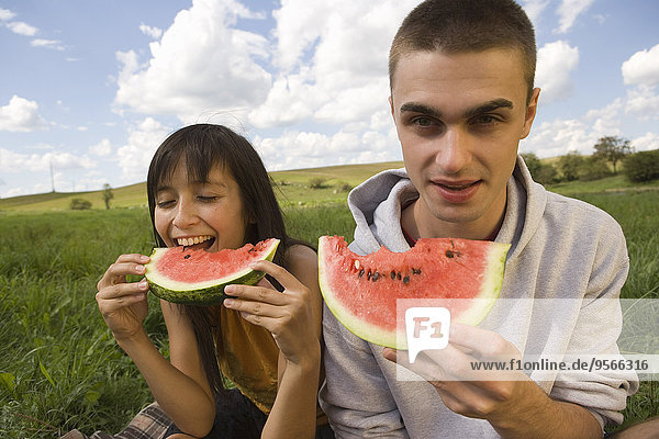 Young couple eating watermelon in field