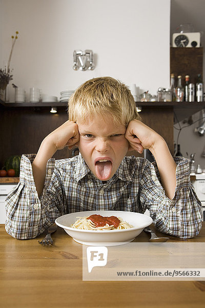 Junge sitzt vor einer Schüssel Spaghetti und streckt die Zunge heraus.