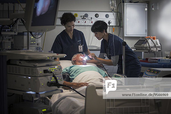 Reife Ärztin und Krankenschwester, die den Hals des Patienten untersucht.