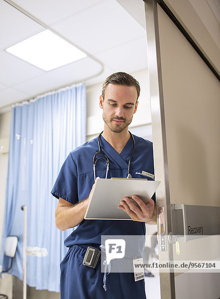 Male doctor standing in doorway  taking notes on clip board in hospital