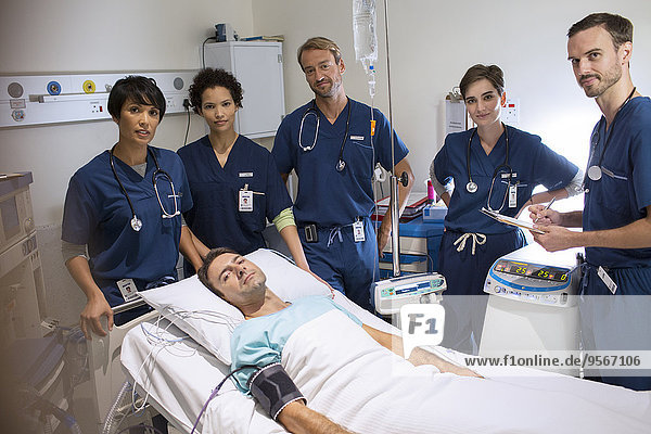 Team of doctors standing around smiling patient lying in bed in intensive care unit