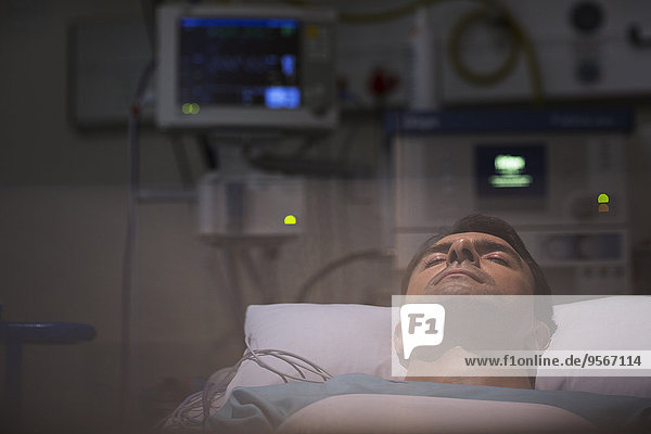Patient lying in bed  surrounded by monitoring medical equipment in intensive care unit