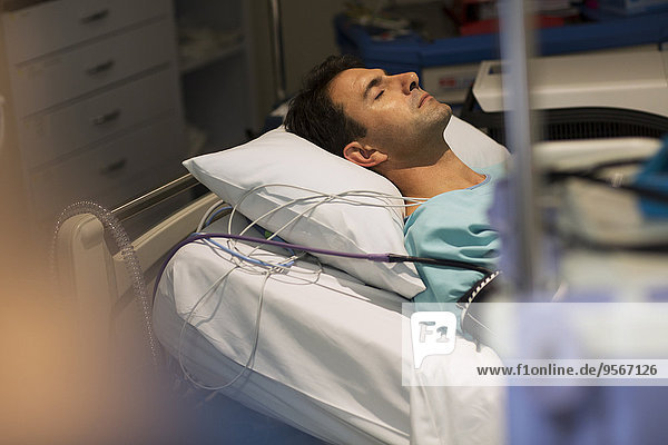 Patient attached to medical monitoring equipment lying in bed in intensive care unit