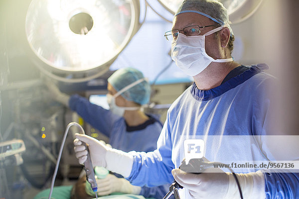Male surgeon holding laparoscopy equipment during surgery in operating theater