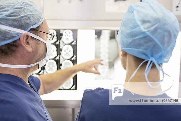 Rückansicht der Chirurgen beim Betrachten der Röntgen- und MRT-Aufnahmen des Patienten im Operationssaal