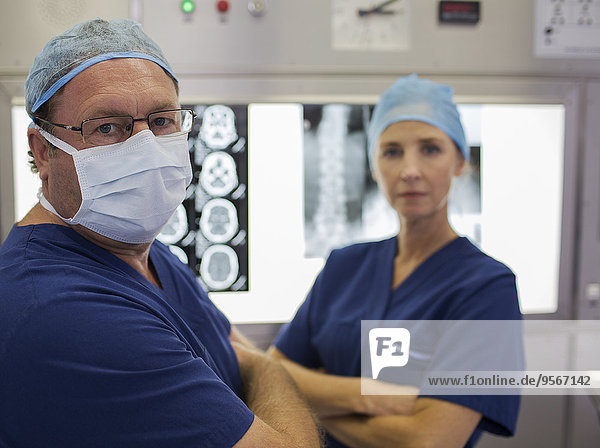 Portrait von Chirurgen mit gekreuzten Armen vor MRT-Scan und Röntgenbild