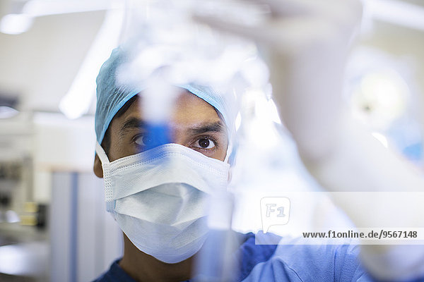 Chirurg mit OP-Maske  Mütze und Handschuhen bei genauer Betrachtung des Infusionstropfens