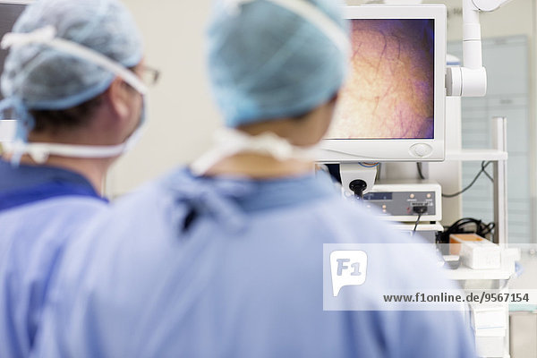 Rückansicht von zwei Chirurgen beim Blick auf den Monitor während der Operation im Operationssaal