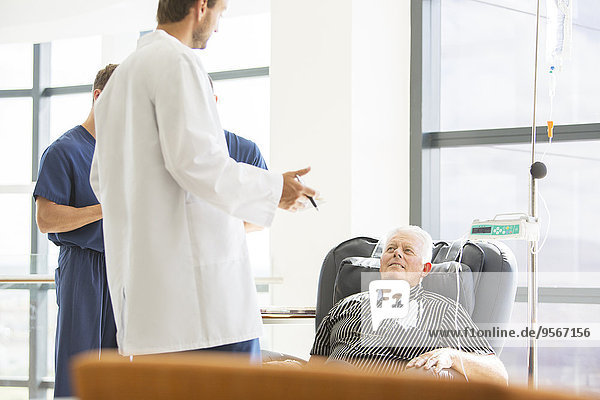 Two doctors talking to senior patient undergoing medical treatment in outpatient clinic
