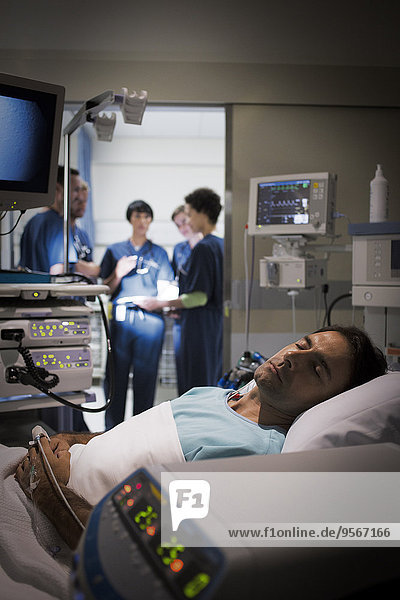 Patient lying in bed in intensive care unit  doctors discussing in background