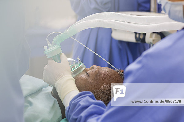 Nahaufnahme des Arztes mit Operationshandschuhen  der die Sauerstoffmaske über den Patienten im Operationssaal hält.
