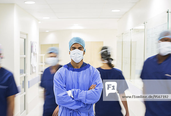 Surgeon with arms crossed  wearing scrubs standing in hospital corridor