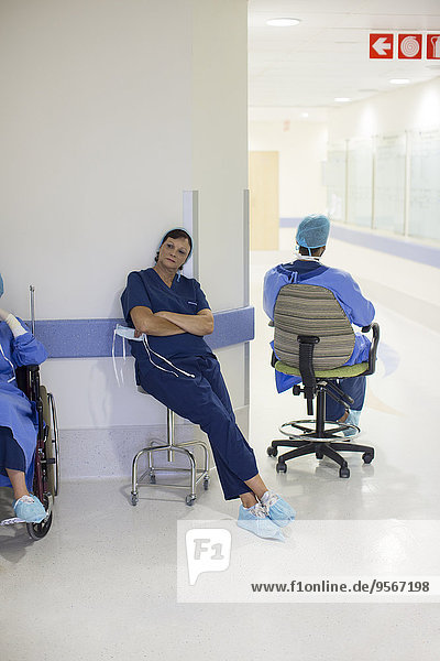 Two doctors wearing surgical clothing resting in hospital corridor