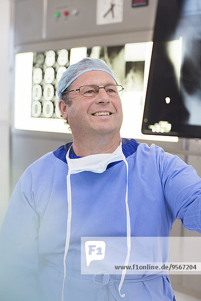 Smiling mature doctor wearing surgical clothing looking at x-ray in hospital