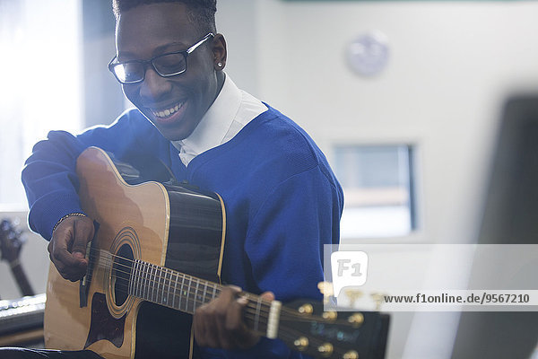 Junge lächelnde Schülerin beim Gitarrespielen im Klassenzimmer