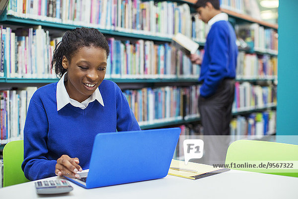 Lächelnde Studentin mit Laptop in der Bibliothek