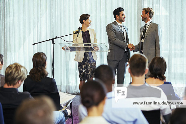 Businessmen shaking hands during presentation in conference room  businesswoman smiling