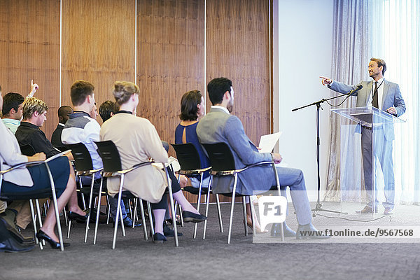 Porträt eines Geschäftsmannes am transparenten Rednerpult vor Publikum im Konferenzraum