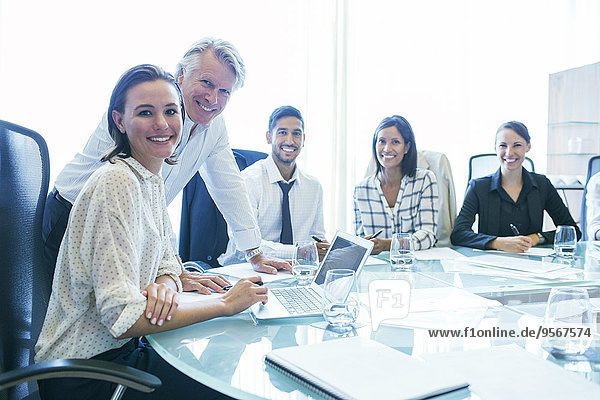 Three businesswomen and two businessmen sitting at conference table  smiling