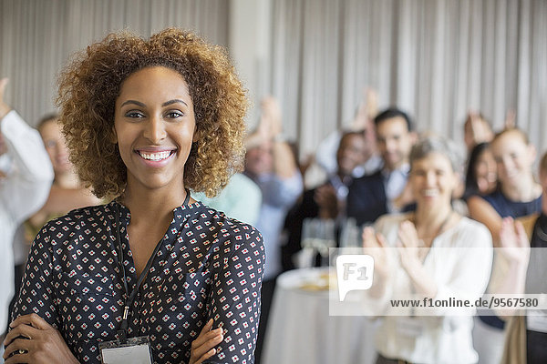 Portrait of smiling young woman in conference room with people applauding in background